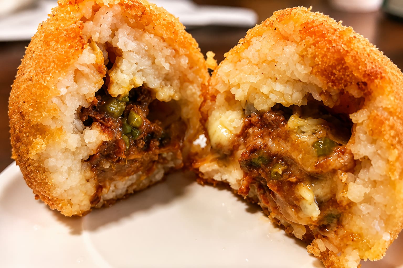 A fried rice ball split in half on a plate, showing ground beef, peas and melted mozzarella inside the rice.