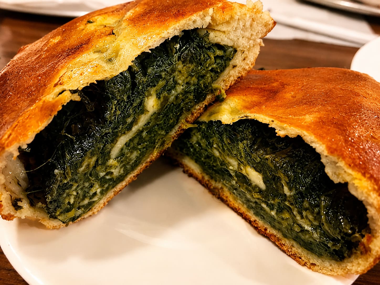 A baked calzone cut in half on a plate, densely filled with spinach and melted cheese.